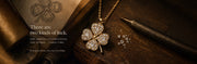 A luxurious image: A four leaf clover shaped real diamond pendant being held by a jewellery makers hand magnified using a magnifying glass. A table with jewellery tools in the background